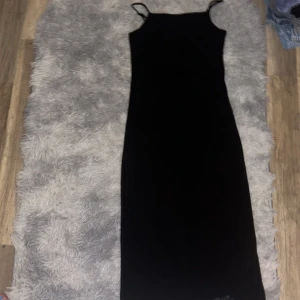 Svart långklänning från Sinsay - En stilren svart långklänning från Sinsay med smala axelband och rak passform. Klänningen är enkel och tidlös, perfekt för dig som gillar minimalistisk stil. Materialet känns mjukt och följsamt mot kroppen.