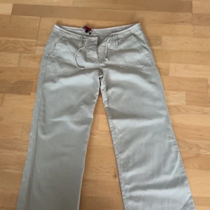 Beiga linnebyxor med snöre - Snygga beiga linnebyxor med raka ben och snörning i midjan. Byxorna har fickor fram och bak, samt knappar på bakfickorna. Perfekta för en avslappnad och stilren look. Sjukt sköna!