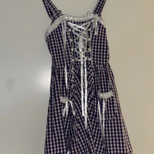 Rutig kortklänning med snörning - Supersöt kortklänning i blåvitt rutigt bomullstyg med vita spetsdetaljer och snörning framtill. Klänningen har breda axelband, fickor med rosetter och en feminin siluett. Perfekt för dig som gillar en lekfull och vintageinspirerad stil. Den har justerbara axelband och är stretchig!! Den passar storlek S och M!<3