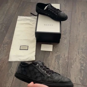 Svarta sneakers från Gucci med monogram - Snygga svarta sneakers från Gucci med klassiskt GG-monogram i tyg och detaljer i skinn. Skorna har rund tå, svarta snören och svarta gummisulor. Perfekta för dig som vill ha en stilren och lyxig look med diskret logga.