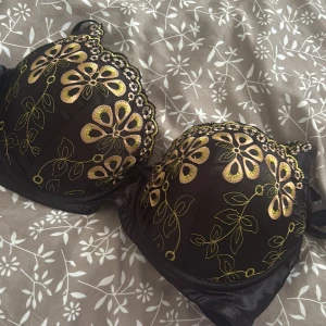 Svart blommig bh  - Snygg svart bh med broderade blommor i gult och beige. Toppen har vadderade kupor och fina broderade detaljer längs kanten. Perfekt för dig som vill ha en unik och färgglad topp under jackan eller till festlooken.