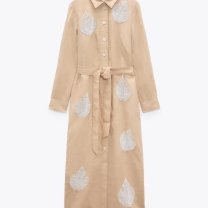 Beige långklänning med pärldetaljer Zara - Långklänning i beige linne från Zara med vita pärlbroderier i bladform. Klänningen har lång ärm, knappar framtill, klassisk krage och ett knytbälte i midjan. Perfekt för dig som gillar unika detaljer och en chill men ändå snygg look. Ny pris var 899kr