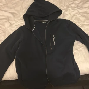 Mörkblå vindjacka från Sail Racing - Mörkblå vindjacka från Sail Racing med huva och dragkedja. Jackan har en stilren look med logga på bröstet och praktisk bröstficka med dragkedja. Perfekt för blåsiga dagar och enkel att matcha med det mesta. Använt 1 gång vill bli av med den köpte en svart istället bra skick.