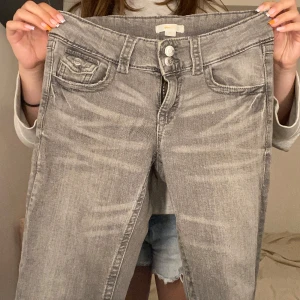 Grå jeans med raka ben - Säljer ett par grå jeans med raka ben och snygga slitningar. Jeansen har klassisk femficksdesign, dubbla knappar i midjan och dragkedja. Perfekta för dig som gillar en avslappnad och stilren look.