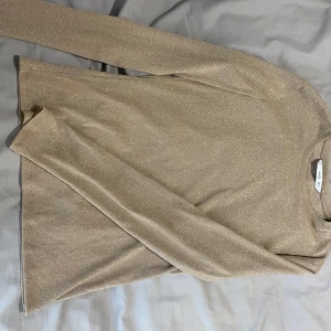Glittrig beige långärmad tröja MNG - Supersnygg beige långärmad tröja från MNG med glittriga inslag. Tröjan har en rak passform och är tillverkad i ett mjukt, stretchigt material som känns bekvämt mot huden. Perfekt när du vill sticka ut lite extra med en diskret men ändå glammig look.