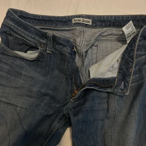 Blå Acne Jeans Hep Pure 32/34 - Säljer ett par klassiska blå Acne Jeans , storlek 32/34. Jeansen har dragkedja, fem fickor och är tillverkade i bomull med lite stretch för extra komfort. Perfekta för en clean och stilren look.