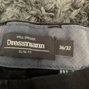 Svarta chinos från Dressmann slim fit - Svarta chinos från Dressmann i slim fit-modell. Klassisk design med snedställda fickor fram och bälteshällor. Perfekta för en clean och stilren look. Mjukt och bekvämt material som passar till det mesta.