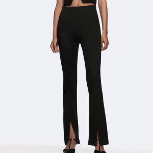 Svarta bootcut byxor med slits - Snygga svarta bootcut byxor med hög midja och slits framtill vid bensluten. Byxorna har en tight passform upptill och är tillverkade i ett stretchigt material som sitter skönt. Perfekta för en trendig och stilren look.