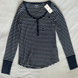 Randig långärmad tröja Hollister - Snygg långärmad tröja från Hollister i marinblått och vitt med klassiskt randigt mönster. Rund halsringning och knappar framtill ger en chill vibe. Tillverkad i mjuk bomull med lite stretch för skön passform. Perfekt för dig som gillar enkel och stilren look. HADE OCKSÅ BYTT MOT EN I SMALL. 