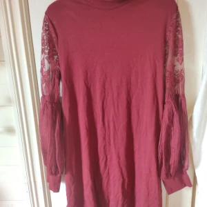 Vinröd klänning med spetsärmar - Röd klänning med ett matchande bälte som går att ta bort helt eller knyta runt midjan. Ärmarna är lite puffiga och klänningen går ner till ungefär knäna på mig som är 164 cm.