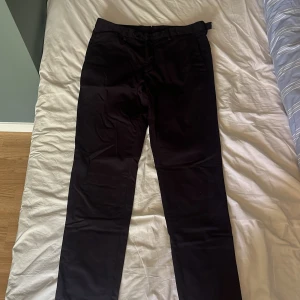 Mörkblåa chinos från Oscar Jacobsson  - Snygga mörblåa chinos med raka ben och klassisk passform. Byxorna har två knappar i midjan, bälteshällor och bakficka med knapp. Materialet är slätt och känns som bomull eller polyester. Perfekta för en stilren look. Knappen har gått sönder som ni ser på bild 3 lämna bud kan tänka mig gå ner i pris 