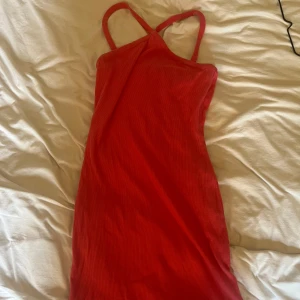 Rosa ribbad klänning - Säljer en rosa ribbad klänning med smala korsade axelband. Klänningen är kort och har en figurnära passform som framhäver siluetten. Materialet är mjukt och stretchigt, perfekt för dig som gillar enkel och stilren design.