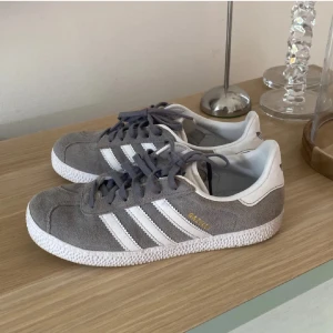 Grå Adidas Gazelle sneakers - Adidas Gazelle – Grå, Oanvända  Säljer ett par helt nya Adidas Gazelle i klassisk grå färg. Tidlösa sneakers som passar till det mesta i garderoben, både vardag och fest. 	•	Storlek: 35,5 (Adidas är stora i storlekar, passar även upp till 37) 	•	Skick: Oanvända, nyskick  Perfekta för dig som vill ha stilrena och bekväma sneakers med ikonisk design.