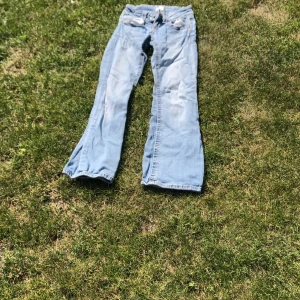 Bootcut jeans i ljusblå denim Gina Tricot - Snygga bootcut jeans från Gina Tricot i ljusblå denim med klassiska fem fickor och dubbla silverknappar fram. Jeansen har kontrastsömmar och breda benslut som ger en retro vibe. Perfekt för dig som gillar avslappnad stil och vill sticka ut lite extra.