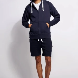 Mörkblå Russenmerch hoodie men vit snörning med prislapp  - Mörkblå hoodie från Russemerch med vit snörning i kragen och praktiska fickor på sidorna. Hoodien har en loose passform och är gjord i mjuk bomull, perfekt för chill dagar. Klassisk stil med enkel design som funkar till shorts eller t-shirt.