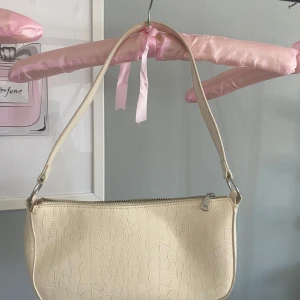 Beige axelväska med croco-mönster - Snygg vit/beige axelväska med croco-präglat mönster och silverfärgad dragkedja. Väskan har en stilren, avlång form och ett smidigt axelband. Perfekt för att bära dina essentials och ger en trendig touch till din outfit.