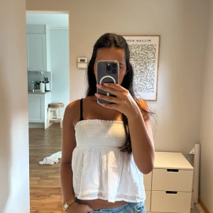 Vit bandeau tubtopp med volang - Säljer en vit bandeau tubtopp med smockad överdel och volang nedtill. Toppen är axelbandslös och har en luftig, flowy passform. Toppen hade nand förut men som tyvär är borta. Skriv för mer bilder. Kan passa mindre storleksr oxå.