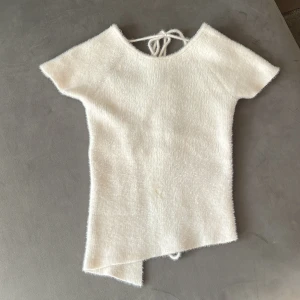 Vit stickad omlottopp från Zara - Superfin vit stickad topp från Zara med korta ärmar och omlottdesign. Toppen har snörning i ryggen som ger en snygg detalj och lite edge. Mjuk och fluffig känsla, perfekt till jeans eller kjol. Asymmetrisk nederkant för extra stilpoäng.