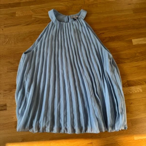 Ljusblå plisserad top H&M - Supersöt ljusblå top från H&M med plisserad design och hög hals. Klänningen är ärmlös och har en luftig, kort passform som ger en chill vibe. Perfekt för varma dagar och när du vill känna dig extra stylish.
