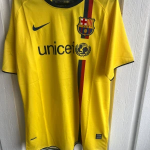 Barcelona Messi 10 gul fotbollströja Nike - Säljer en gul FC Barcelona fotbollströja från Nike med Messi 10 på ryggen. Tröjan har korta ärmar, svarta detaljer vid krage och ärmslut, samt klubbmärke och UNICEF-logga på bröstet. Materialet är lätt och andas, perfekt för match eller träning.