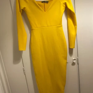 Gul långklänning från Boohoo - Snygg gul långklänning från Boohoo med v-ringad hals och långärmade ärmar. Klänningen har en figurnära passform och är tillverkad i mjukt polyester-material. Perfekt för dig som vill sticka ut med en färgstark look.