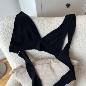 Svart ribbstickad knyt-topp från Mango - Svart knyt-topp från Mango i ribbad, stretchig bomull. Snygg V-ringad design med breda axelband och croppad passform som ger en cool och trendig look. Perfekt att styla med jeans eller kjol för en edgy vibe.