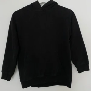 Svart hoodie från Spreadshirt - Svart hoodie från Spreadshirt med stor huva och magficka. På ryggen finns ett coolt geometriskt tryck i vitt. Tröjan har långa ärmar och är gjord i mjuk bomull, perfekt för chill dagar. Passar dig som gillar enkel stil med en twist.