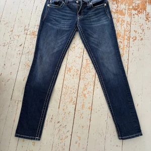Miss Me blå jeans med broderade fickor - Säljer ett par snygga blå jeans från Miss Me med raka ben och coola broderade detaljer på bakfickorna. Jeansen har kontrastsömmar och klassisk femficksdesign. Perfekt för dig som gillar statement-plagg och vill sticka ut lite extra.