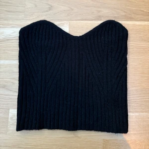 Tubtopp svart  - Svart tubtopp med en vågig halslinje och ribbad textur. Perfekt för en utekväll eller en somrig dag. Storlek S