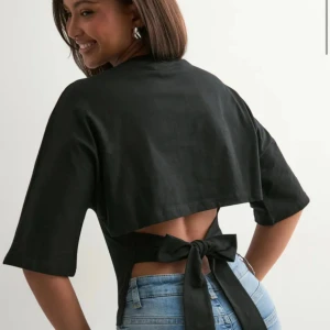 Svart topp med knyt i ryggen - Säljer en svart omlottopp med halvlånga ärmar och snygg knytning i ryggen som ger en öppen rygg-effekt. 