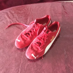 Sneakers från Puma - Snygga röda sneakers från Puma med klassisk vit logga och sidostripes. Skorna har snörning och en platt sula. Ovandelen är i textil och mocka, medan sulan är i gummi. Perfekt för dig som gillar sportig stil och vill sticka ut med färg.