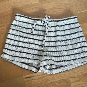 Randiga stickade shorts med snörning - Säljer ett par mysiga stickade shorts med svartvita ränder och snörning i midjan. De har en loose passform och är perfekta för chill dagar. Materialet är mjukt och ger en skön känsla mot huden. Passar dig som gillar en avslappnad och cool stil.