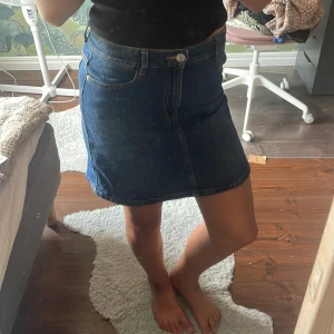 Blå jeanskjol från Lindex - Klassisk blå jeanskjol från Lindex med femficksmodell, bälteshällor och knapp framtill. Kjolen är i bra skick, skriv för fler bilder💗