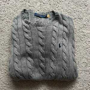 Grå kabelstickad tröja Polo Ralph Lauren - Säljer en snygg grå kabelstickad tröja från Polo Ralph Lauren med klassisk rund hals och broderad marinblå logga på bröstet. Tröjan är i mycket bra skick & är defektfri. Pris ej hugget i sten, kontakta vid minsta fråga!