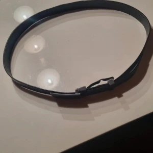 Svart skärp från Gucci i skinn - Snyggt svart bälte från Gucci, tillverkat i Italien. Bältet är gjort av äkta skinn och har en stilren, rektangulär metallspänne med Gucci-loggan ingraverad. Perfekt för dig som vill ha en klassisk och exklusiv accessoar med lyxig känsla.