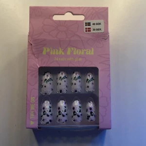 Pink Floral lösnaglar med lim - Säljer ett set med 24 lösnaglar i oval form med blommigt mönster. Naglarna är ljusrosa med gröna och svarta detaljer och kommer med lim. Perfekt för dig som vill ha snygga och unika naglar snabbt.