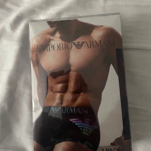 Svarta Emporio Armani kalsonger - Säljer ett 3-pack svarta kalsonger från Emporio Armani med stretchig bomullskvalitet. De har bred resår med logotyp och ikonisk örn i silver och regnbågsfärger framtill. Snygga och bekväma med modern passform, perfekta för dig som gillar stilrena underkläder.