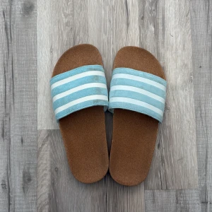 Randiga blå sandaler med platt sula - Tofflor från adidas i trämaterial. Lite smutsiga och därför säljs dem billigt. Skulle gissa strl 38 pris går att diskutera 