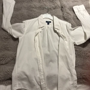 Vit skjorta från GANT, 146/152 cm - Klassisk vit skjorta från GANT med krage och långa ärmar. Skjortan har knappar framtill och vid ärmsluten. Tillverkad i mjuk bomull, perfekt för dig som gillar stilrena och enkla plagg. Passar dig som är 11-12 år och vill ha en clean look.