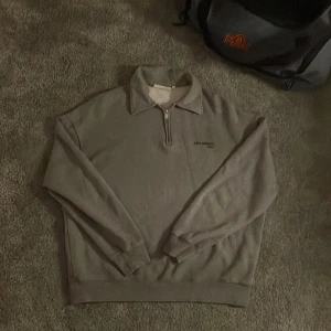 Grå half zip tröja Axel Arigato - Grå långärmad tröja från Axel Arigato med halv dragkedja och krage. Stilren design med diskret logga på bröstet. Mjuk och skön bomullskvalitet, perfekt för chill dagar. Passar dig som gillar minimalistisk och clean stil.