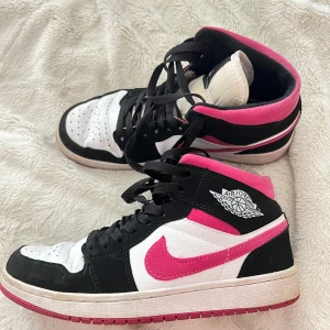 Nike Air Jordans med rosa detaljer - Säljer ett par Nike Air Jordans med svart, vitt och rosa färg. Skorna har högt skaft, svart snörning och den klassiska Air Jordan-loggan på sidan. Rosa swoosh och innersida ger en snygg kontrast till det svarta och vita.