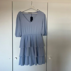 Ljusblå volangklänning med v-ringning - Supersöt ljusblå klänning med v-ringad hals och trekvartsärmar. Kjolen har flera lager volanger som ger en flowy känsla. Perfekt för sommarens alla tillfällen! Den är helt ny och lappen är fortfarande kvar, säljer då den inte har kommit till användning💕🫧✨
