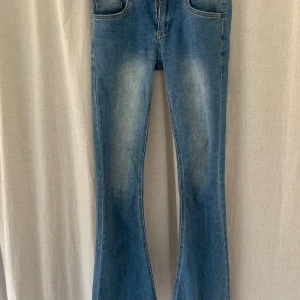 Blå bootcut jeans - Snygga blå bootcut jeans med klassisk femficksdesign och lätt slitna detaljer framtill. Jeansen har normal passform upptill och utsvängda ben, perfekt för en trendig look. Stängs med dragkedja och knapp.