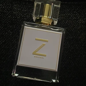 Z Sweden parfym - Exklusiv parfym från Z Sweden med stilren, genomskinlig glasflaska och guldiga detaljer. Flaskan har en fyrkantig form och ett elegant lock. Parfymen levereras i en svart och guldig förpackning med modern design. Tillverkad i Sverige.