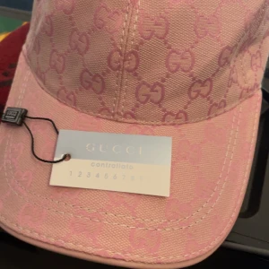 Rosa keps från Gucci med monogram - Säljer en rosa keps från Gucci med klassiskt GG-monogram i hela tyget. Kepsen har böjd skärm och justerbart spänne bak. Perfekt accessoar för att lyfta din stil med en lyxig touch.