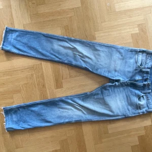Levis ljusblå jeans - Klassiska Levis jeans i ljusblå tvätt med raka ben och råa benslut. Jeansen har fem fickor, knappgylf och tydlig Levis-lapp bak i midjan. Perfekta för en avslappnad och tidlös stil.