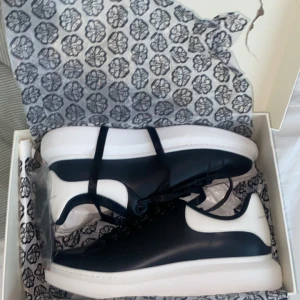 Svart vita skor från märket Alexander maqueen  - Säljer ett par snygga svarta och vita sneakers från Alexander McQueen med klassisk chunky vit sula och svarta skosnören. Skorna har en stilren design med vit hälkappa där loggan syns tydligt. Perfekta för dig som gillar statement sneakers. De har är helt oanvända och perfekta för speciella tillfällen.