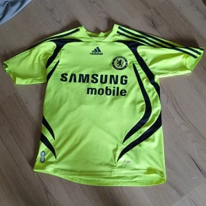 Chelsea tröja, John Terry - Säljer en limegrön Chelsea FC bortatröja från säsongen 2008/09 med svart mönster, Adidas-logga och Samsung Mobile sponsortryck. Tröjan har korta ärmar, klubbmärke på bröstet och namn samt nummer (Terry 26) på ryggen. Såklart riktig, skick 9/10