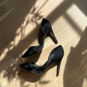 Svarta pumps med spetsig tå från NLY - Säljer ett par klassiska svarta pumps från NLY med spetsig tå och hög klack. Skorna är i syntetmaterial och har en elegant, stilren design som passar perfekt till många olika outfits. De är använda utomhus och har därför defekter där av de billiga priset. 