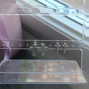 Två par korsformade örhängen i silverfärg - Säljer två par korsformade örhängen i silverfärg. Ett par är dekorerade med glittrande stenar och det andra paret är enkla och stilrena. Perfekta för dig som gillar att mixa och matcha smycken.